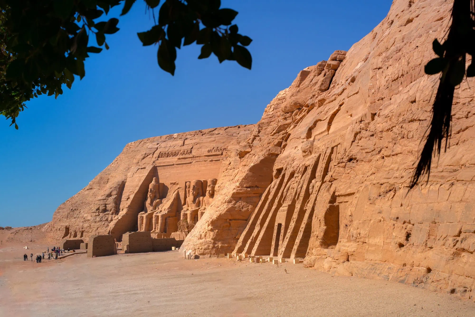 Ancient Abu Simbel temples carved into sandstone cliffs with tourists exploring the site