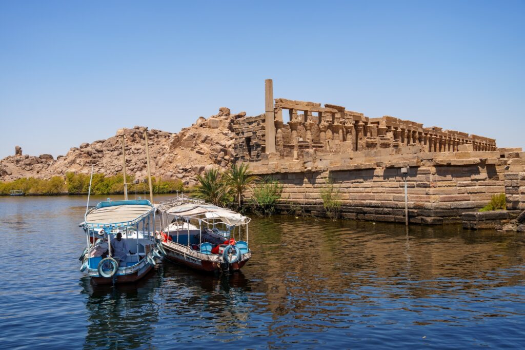Boats moored along the Nile near the Philae Temple Complex with temple structures on the island, Aswan