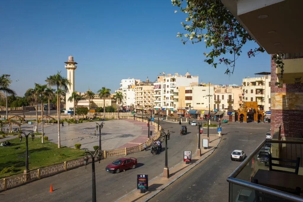 Road traffic in downtown Luxor Temple Square with the minaret of Ahmed Negm Mosque and flowers hanging from a balcony, Luxor