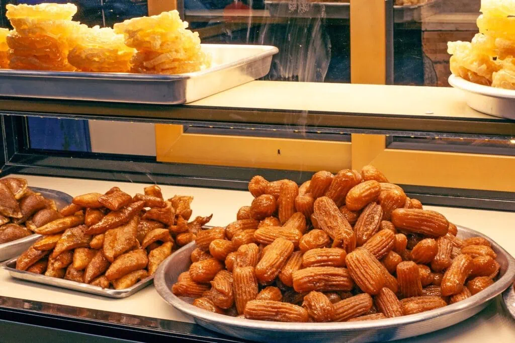 Display of fresh Egyptian sweets arranged on trays at a street market stall after sunset, Luxor Market, Luxor