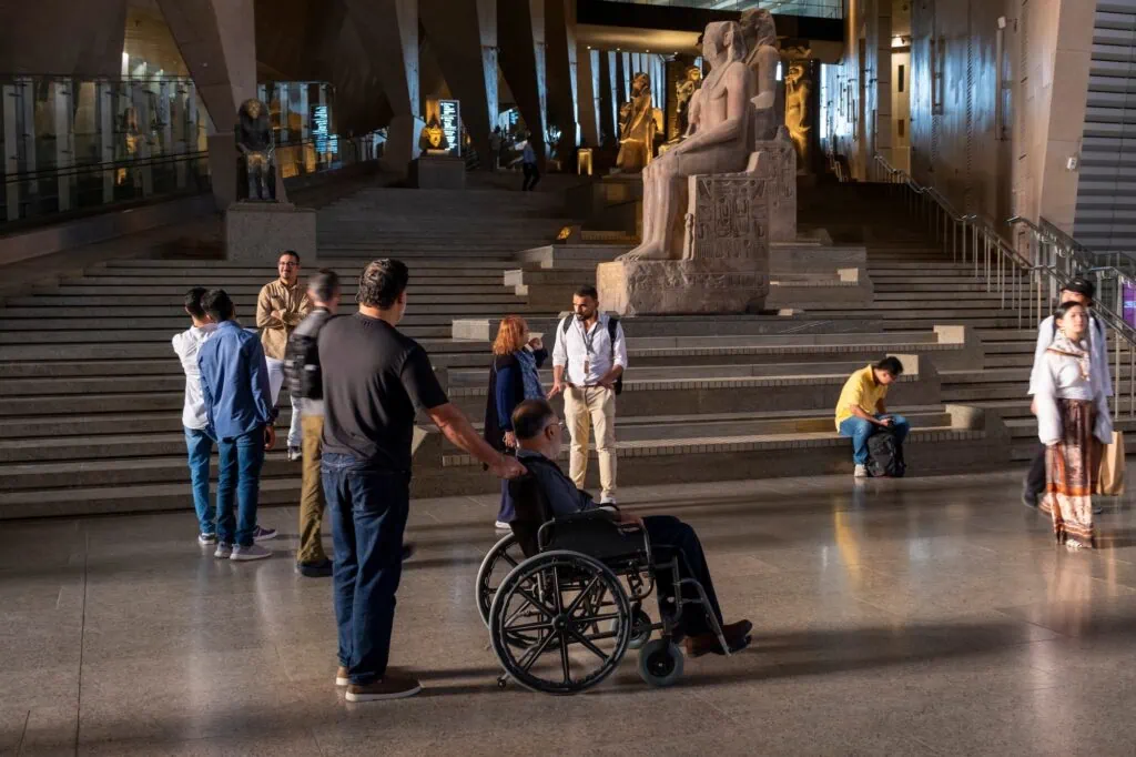 Man using a wheelchair with an assistant in the large atrium space of the Grand Egyptian Museum