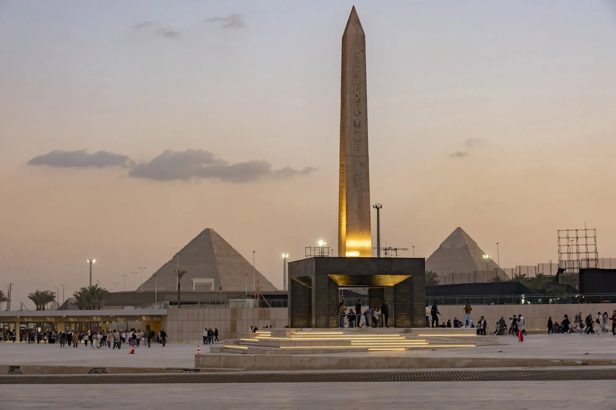 Grand Egyptian Museum at dusk with illuminated obelisk and Giza pyramids in background