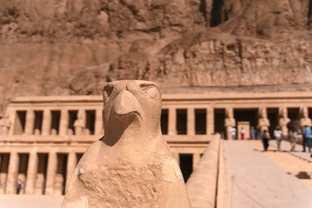 Horus statue at the entrance of the mortuary temple of Hatshepsut with stone terraces and cliffs behind, Luxor