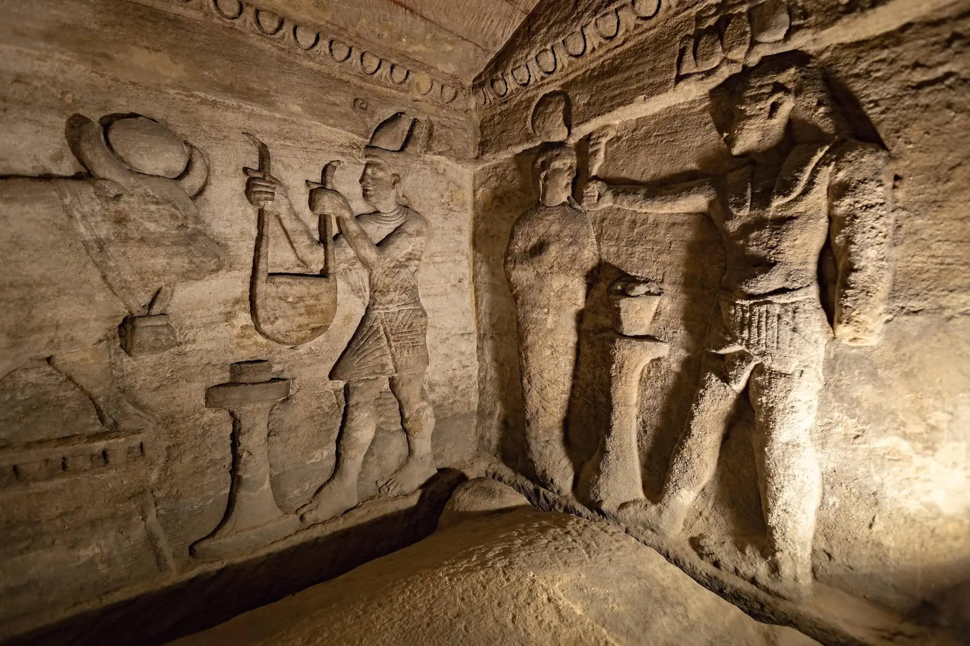 Ancient underground burial chamber with carved Egyptian reliefs and hieroglyphic decorations