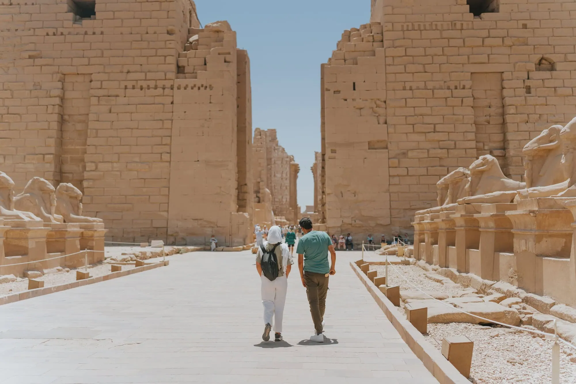 Tourists walking through Karnak Temple complex with sphinx statues