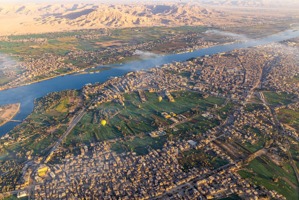 Panoramic view of the Nile River, city buildings, and surrounding farmland seen from a hot air balloon over Luxor, Luxor