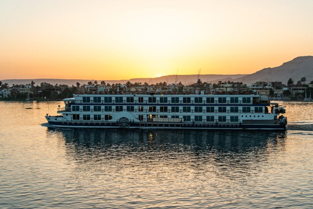Cruise ship sailing along the Nile River at sunset with reflections on the water, Nile River, Aswan
