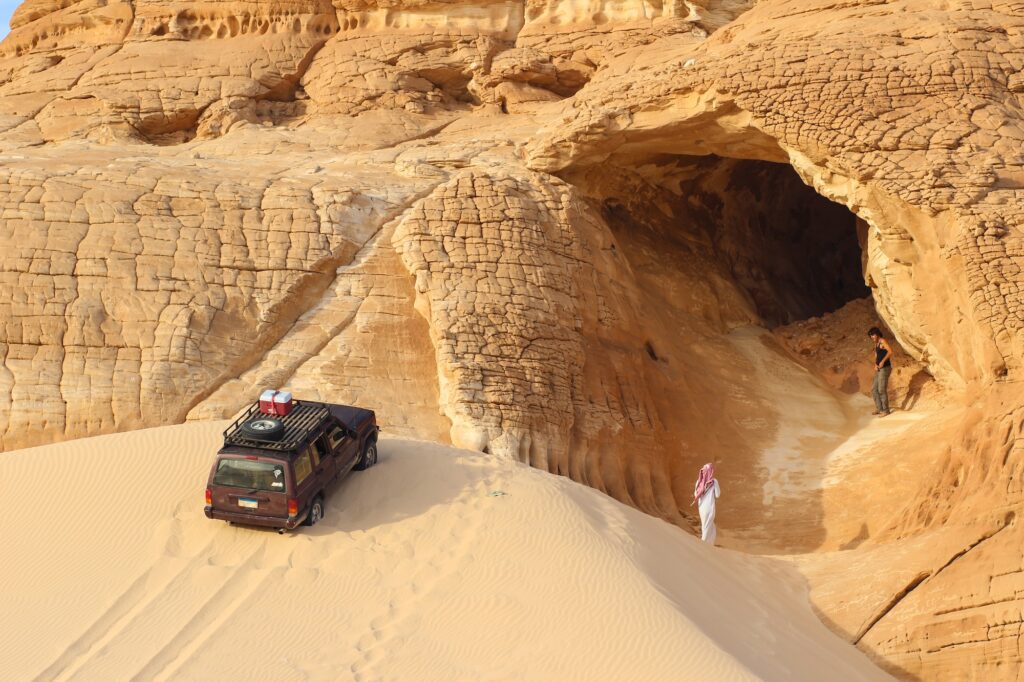 Gilf Kebir Plateau desert landscape with sand dune, sandstone mountain formations, and off-road vehicle, Gilf Kebir