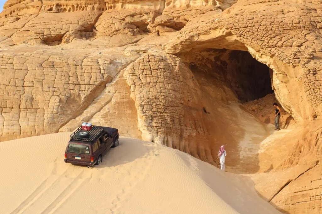 Gilf Kebir Plateau desert landscape with sand dune, sandstone mountain formations, and off-road vehicle, Gilf Kebir