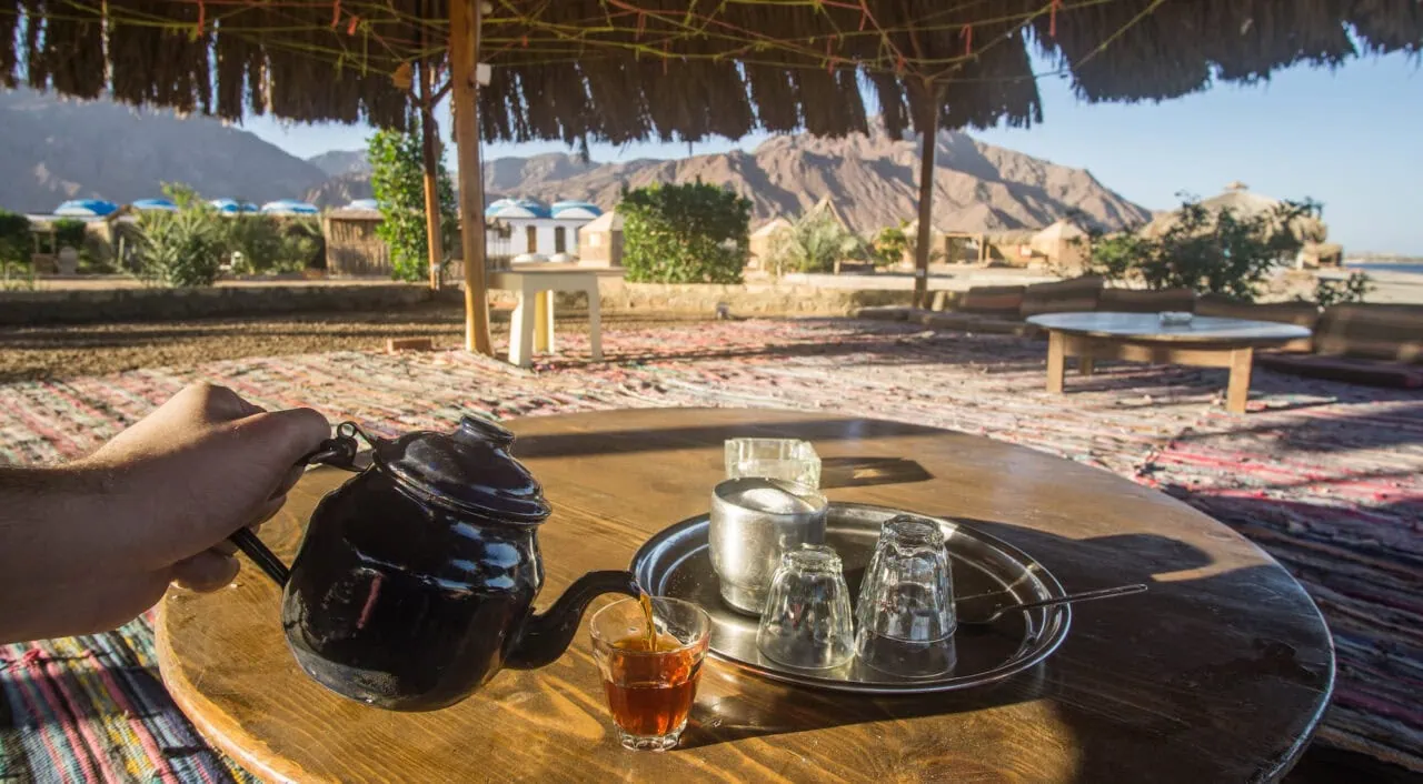Teapot and tea glasses on a wooden table in a big open Bedouin tent with an amazing view of the mountains and the beach , captured in a beach camp around Nuweiba in South Sinai , Egypt