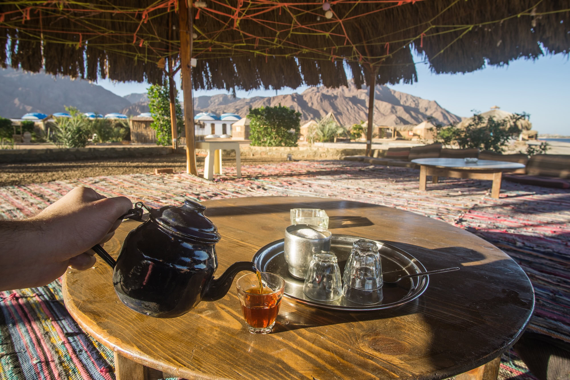 Teapot and tea glasses on a wooden table in a big open Bedouin tent with an amazing view of the mountains and the beach , captured in a beach camp around Nuweiba in South Sinai , Egypt