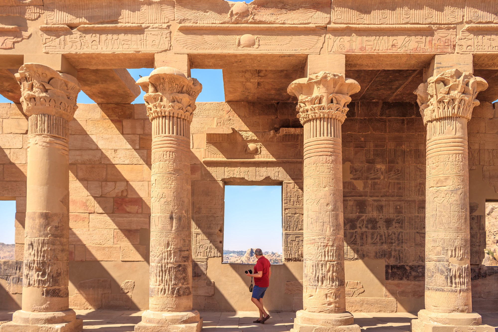 Tourist exploring ancient Egyptian temple columns at Philae with hieroglyphic carvings