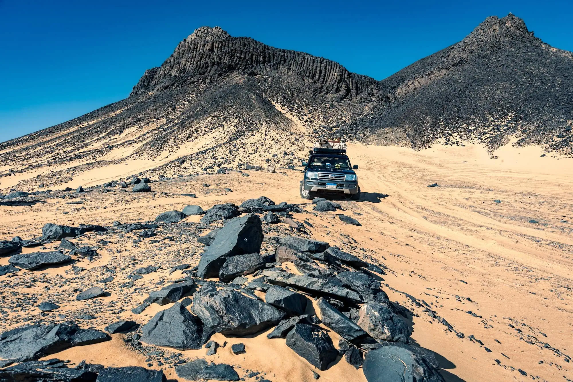 4x4 vehicle driving through Egypt's Black Desert with dark volcanic rocks and sandy terrain