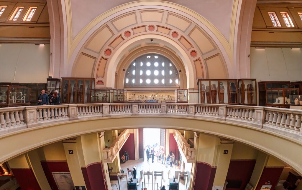 Interior gallery and upper balcony of the Egyptian Museum with display cases and visitors, Cairo