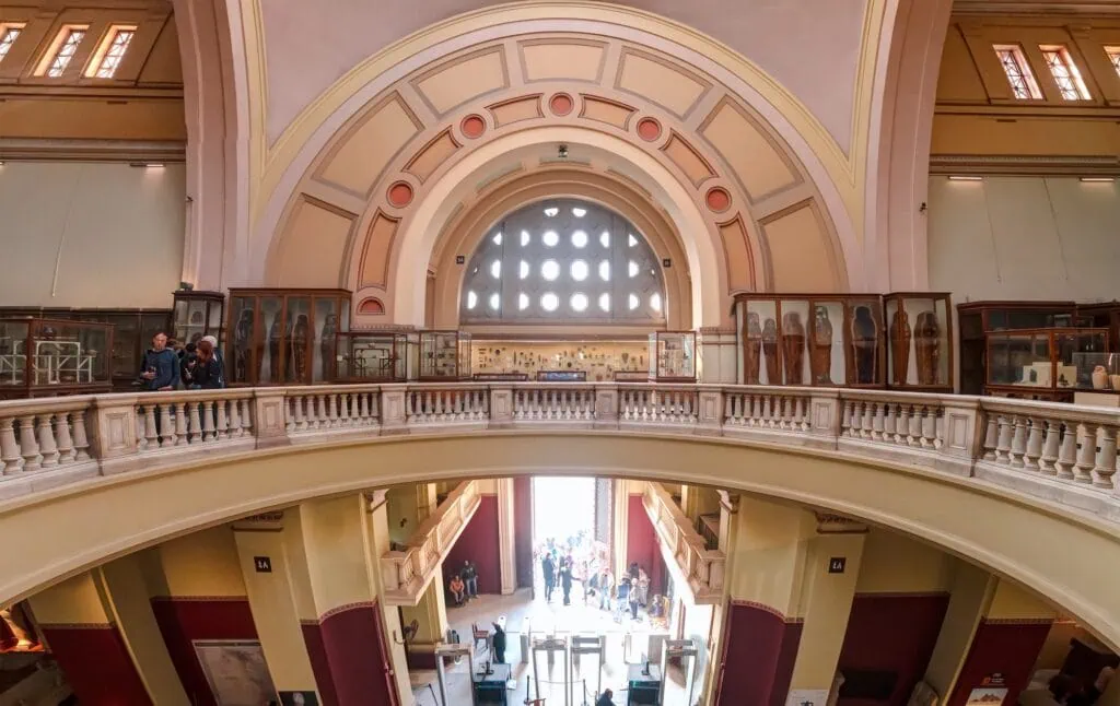 Interior gallery and upper balcony of the Egyptian Museum with display cases and visitors, Cairo