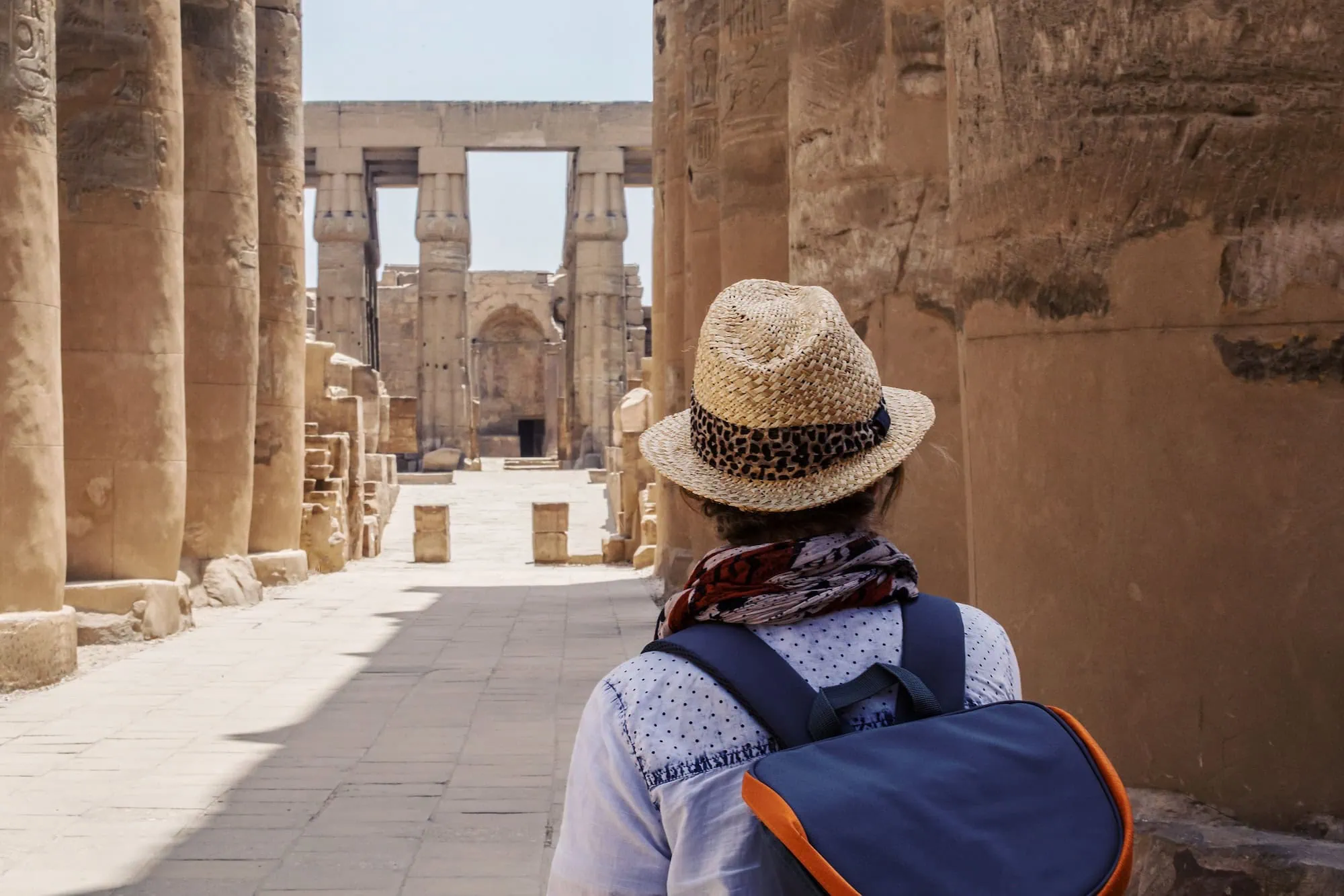 Tourist with backpack sitting and viewing ancient Egyptian temple columns at Karnak