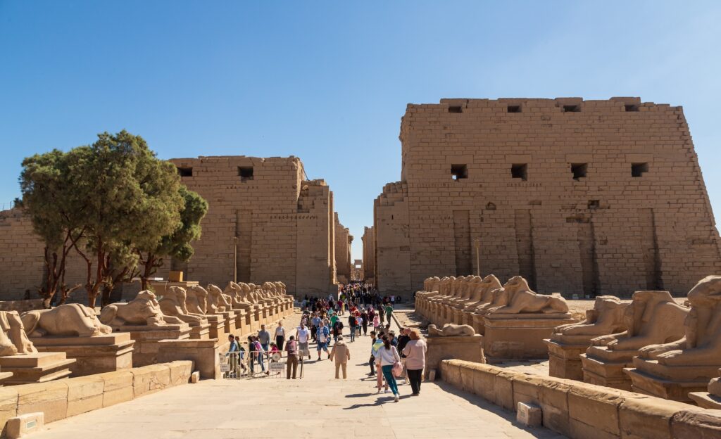 Tourists walking along the Avenue of Sphinxes with temple ruins in the background at Karnak Temple, Luxor