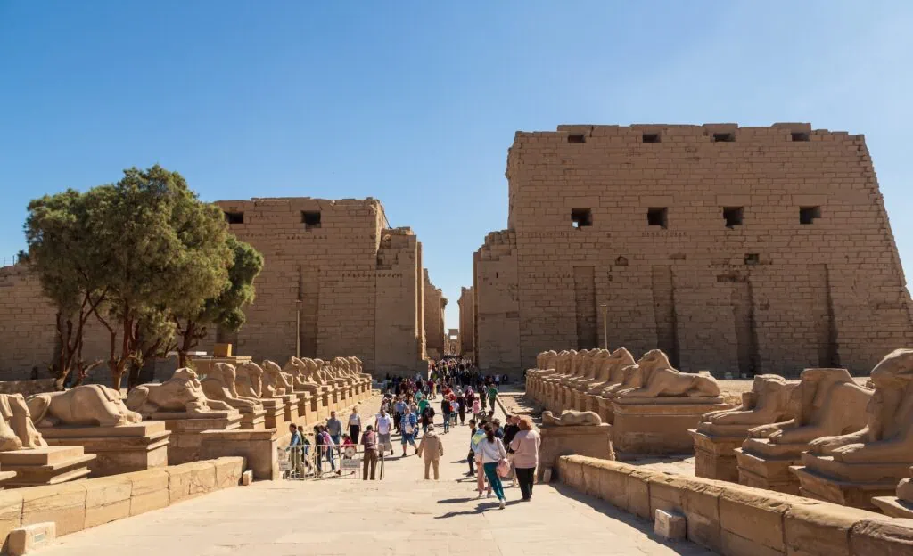 Tourists walking along the Avenue of Sphinxes with temple ruins in the background at Karnak Temple, Luxor