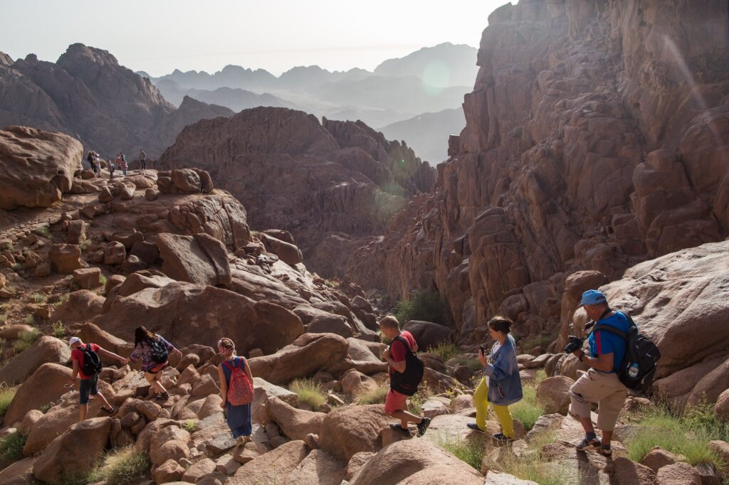 Travelers walking along the rocky trail on Mount Sinai with surrounding red rock formations, Saint Catherine