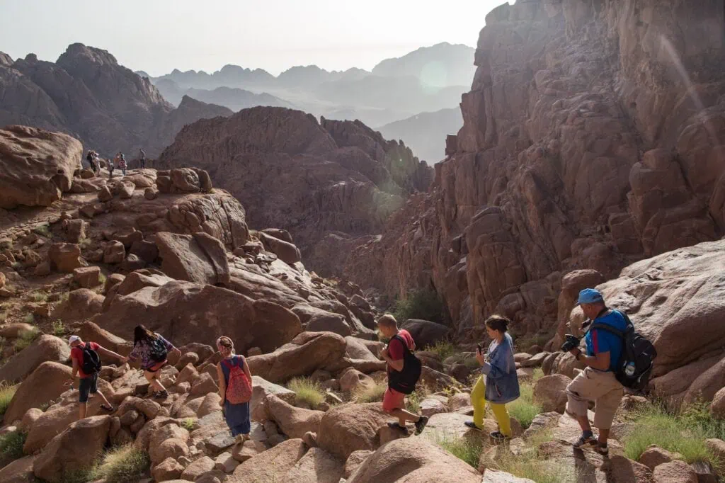 Travelers walking along the rocky trail on Mount Sinai with surrounding red rock formations, Saint Catherine