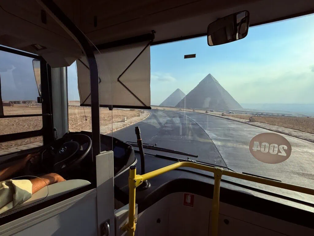 View from a modern bus approaching the pyramids with roadway and transit infrastructure visible, Pyramids of Giza, Giza