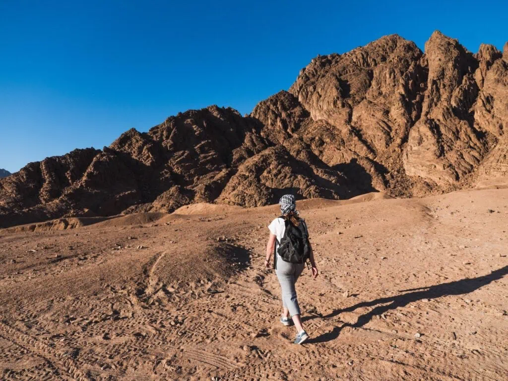 Girl walking across rocky desert terrain with mountain backdrop at Sinai Desert, Sharm el Sheikh