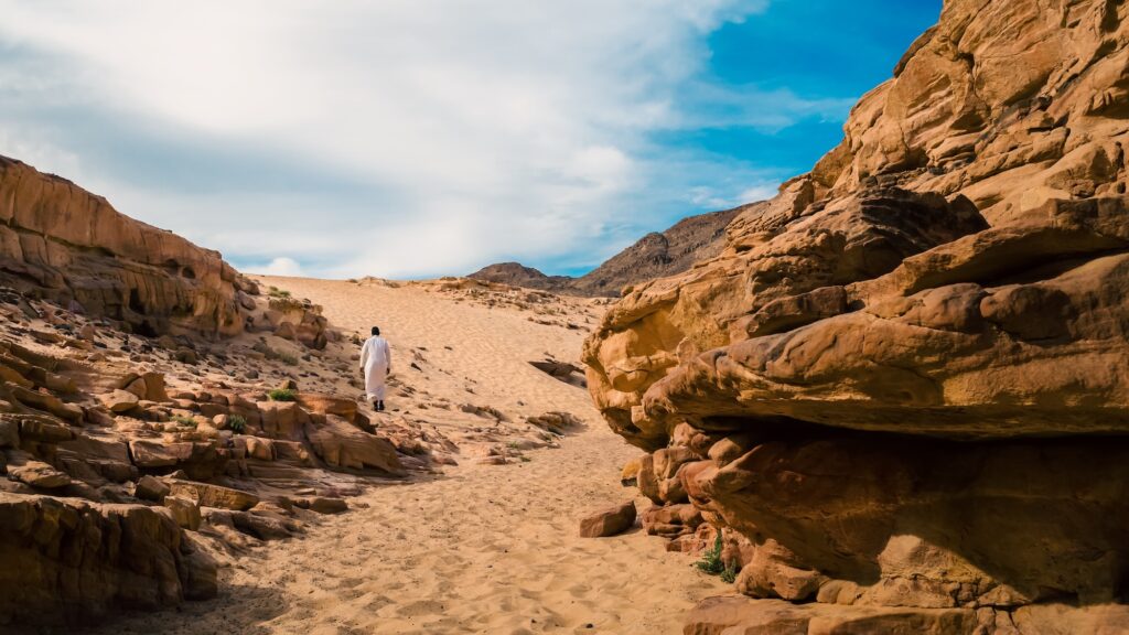 Man in traditional white clothing walking through the narrow colored canyon walls, Dahab