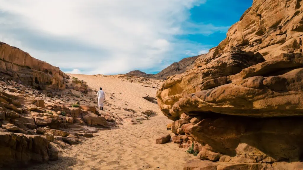 Man in traditional white clothing walking through the narrow colored canyon walls, Dahab