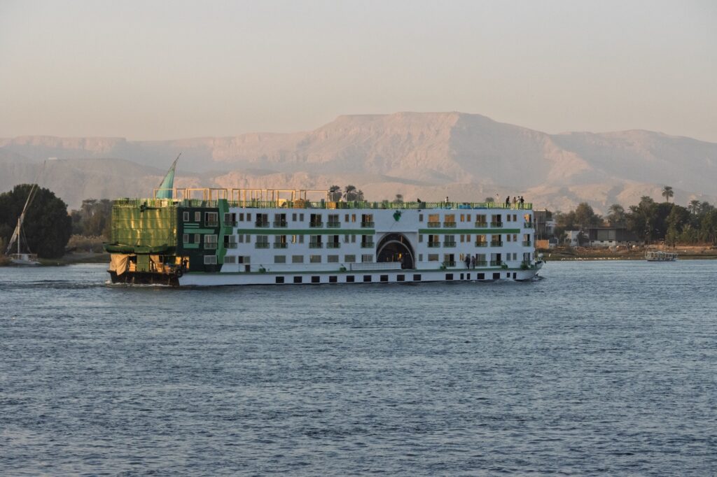 Large cruise ship sailing along the Nile River with riverbanks visible near Luxor, Luxor