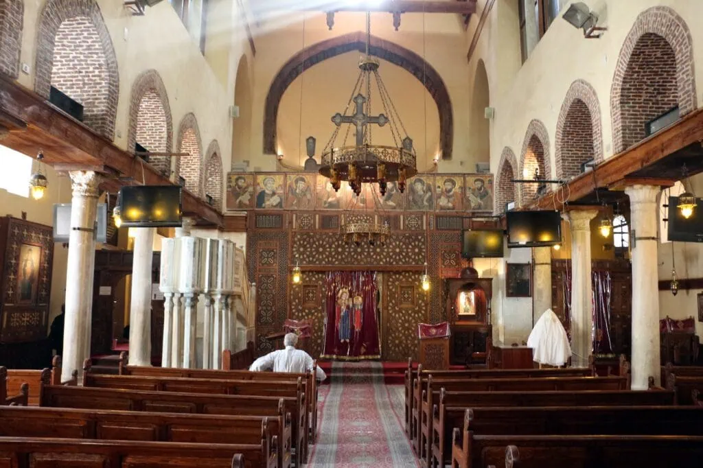 An interior view with ornate architectural details, carved iconostasis, wooden pews, and decorative elements inside Saint Barbara Church, Cairo