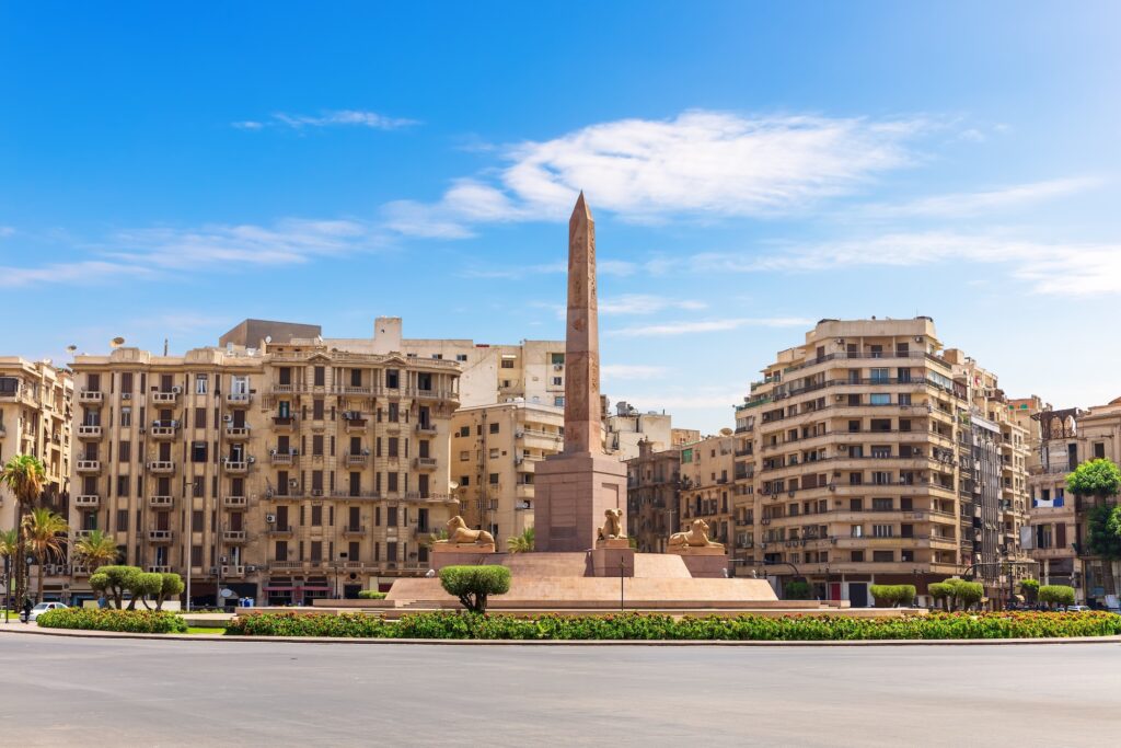 Ramses II obelisk standing in Tahrir Square with surrounding buildings and traffic, Cairo