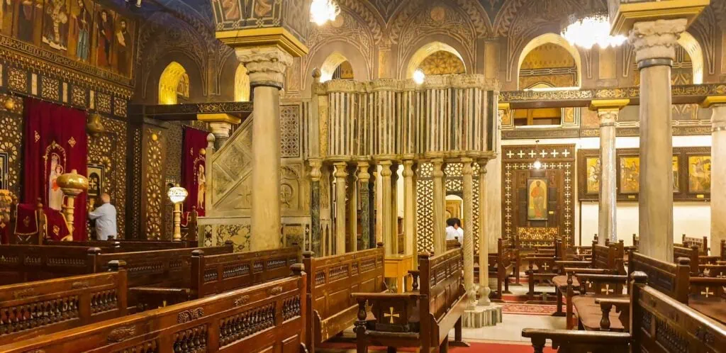 An interior view showing the prayer hall with wooden balconies, central bimah, and decorative ark inside the Ben Ezra Synagogue, Cairo