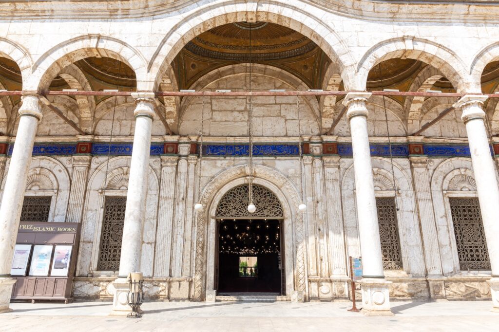 Carved Arabic facade with ornamental details and white courtyard columns at the entrance of the prayer hall of Muhammad Ali Mosque, Cairo