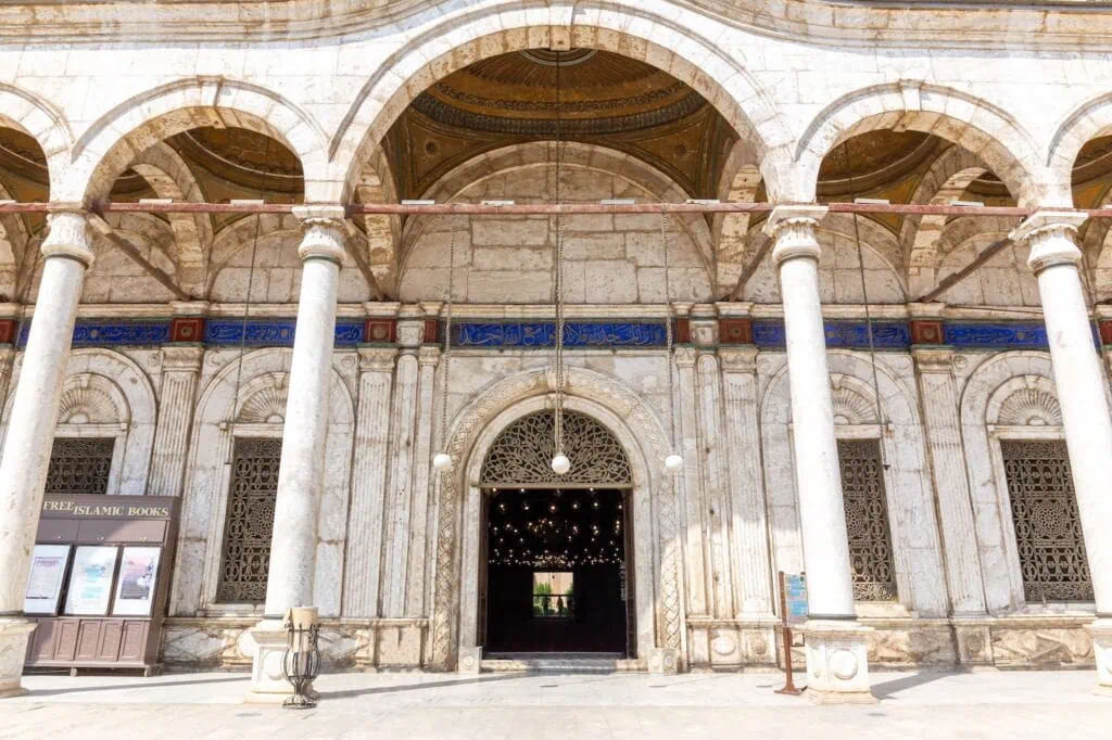 Carved Arabic facade with ornamental details and white courtyard columns at the entrance of the prayer hall of Muhammad Ali Mosque, Cairo