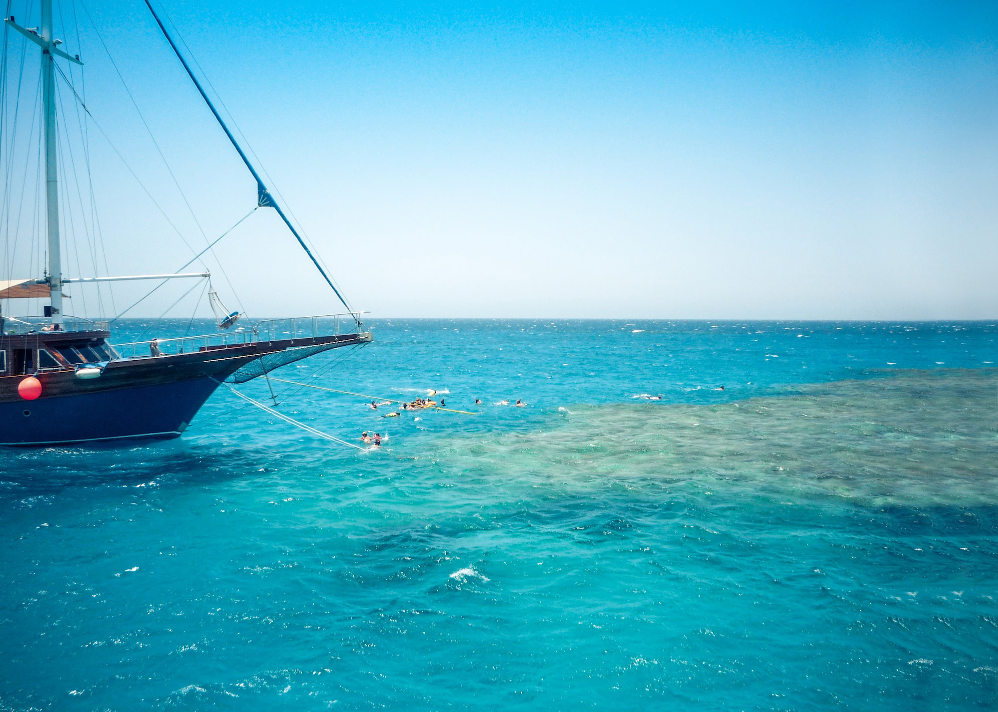 Tourists swimming and snorkeling around a sailboat in the crystal clear turquoise waters of the Red Sea