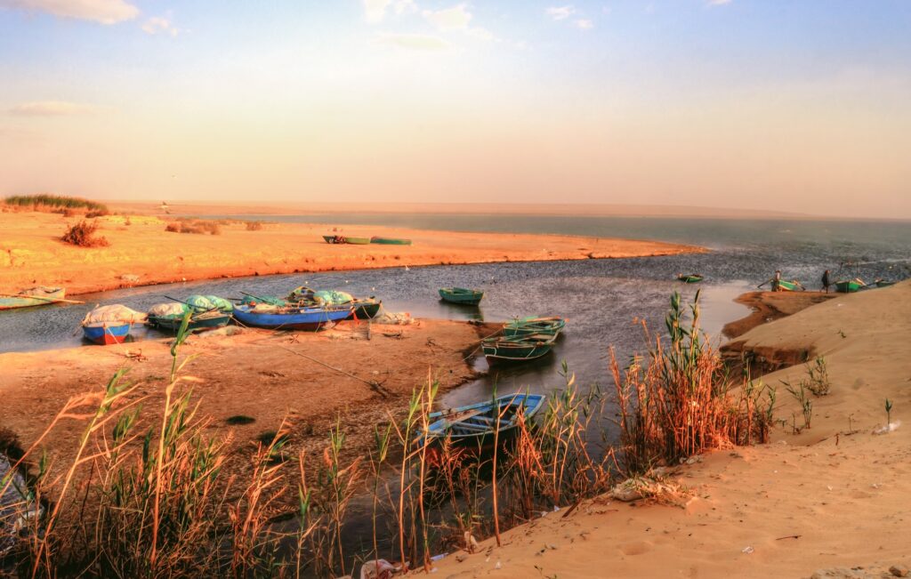 Small boats docked along the calm shoreline of a desert lake in Wadi El Rayan, Fayoum