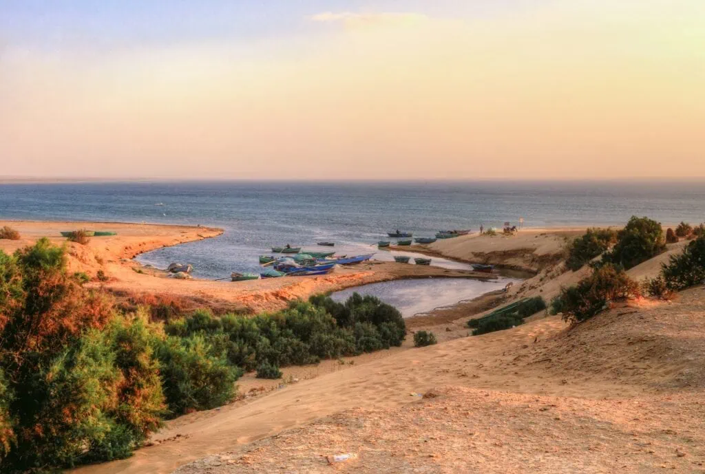 View of water bordered by desert sands and green vegetation across the landscape at Wadi El Rayan, Fayoum