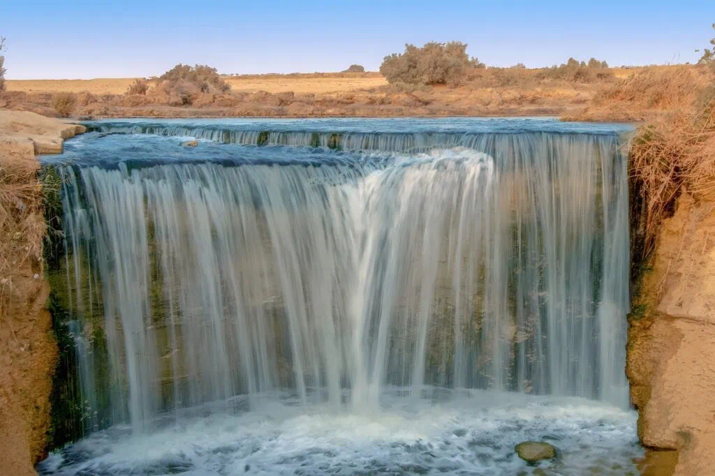 Desert lake and cascading waterfall surrounded by sandy terrain at Wadi El Rayan, Fayoum