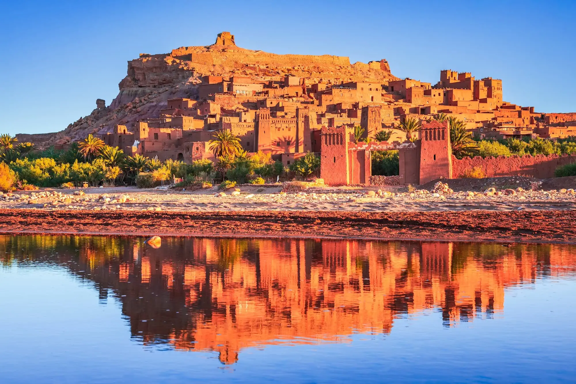 Ait Benhaddou kasbah at sunset with golden lighting and water reflection