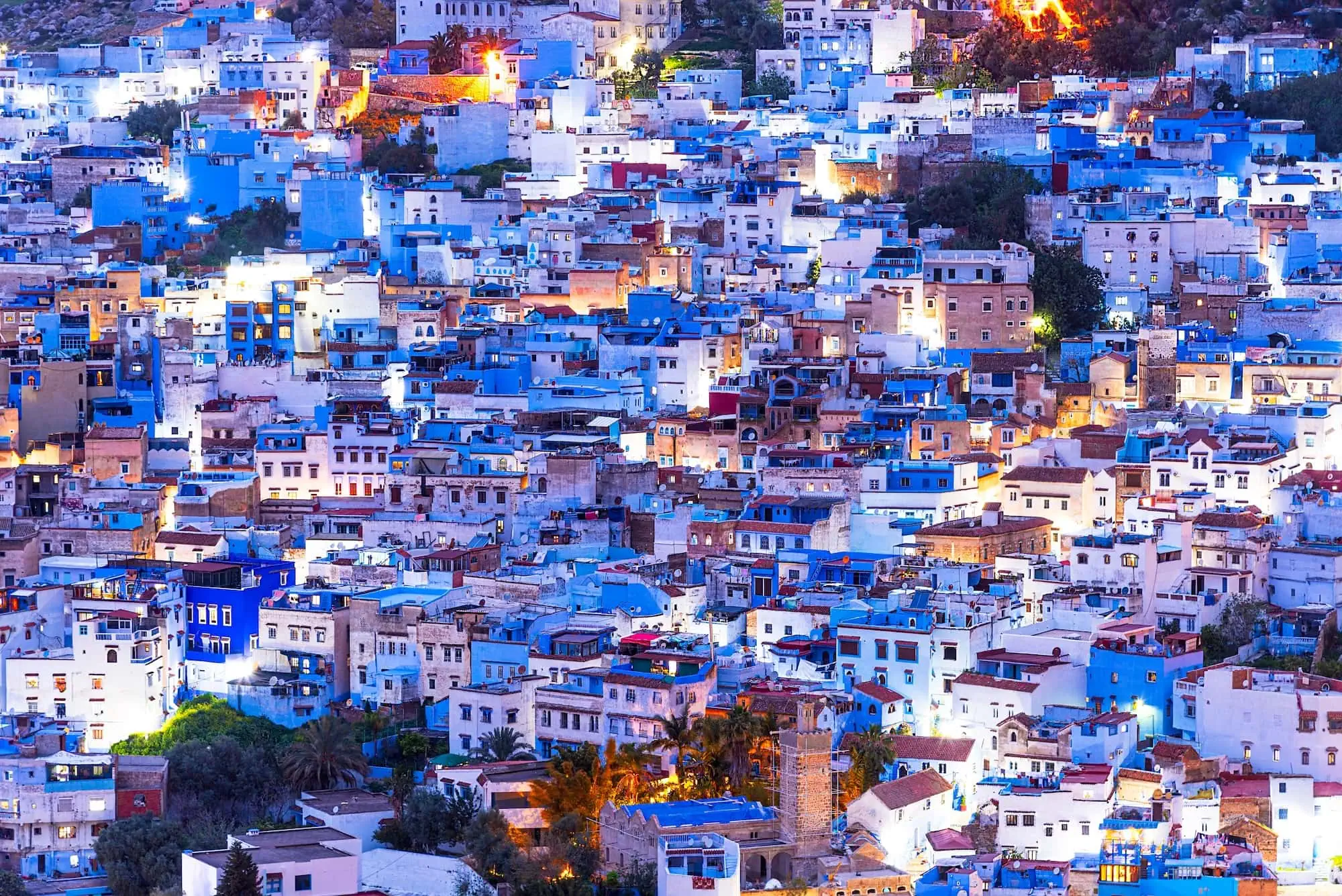 Panoramic view of Chefchaouen's blue-painted medina buildings cascading down hillsides at golden hour