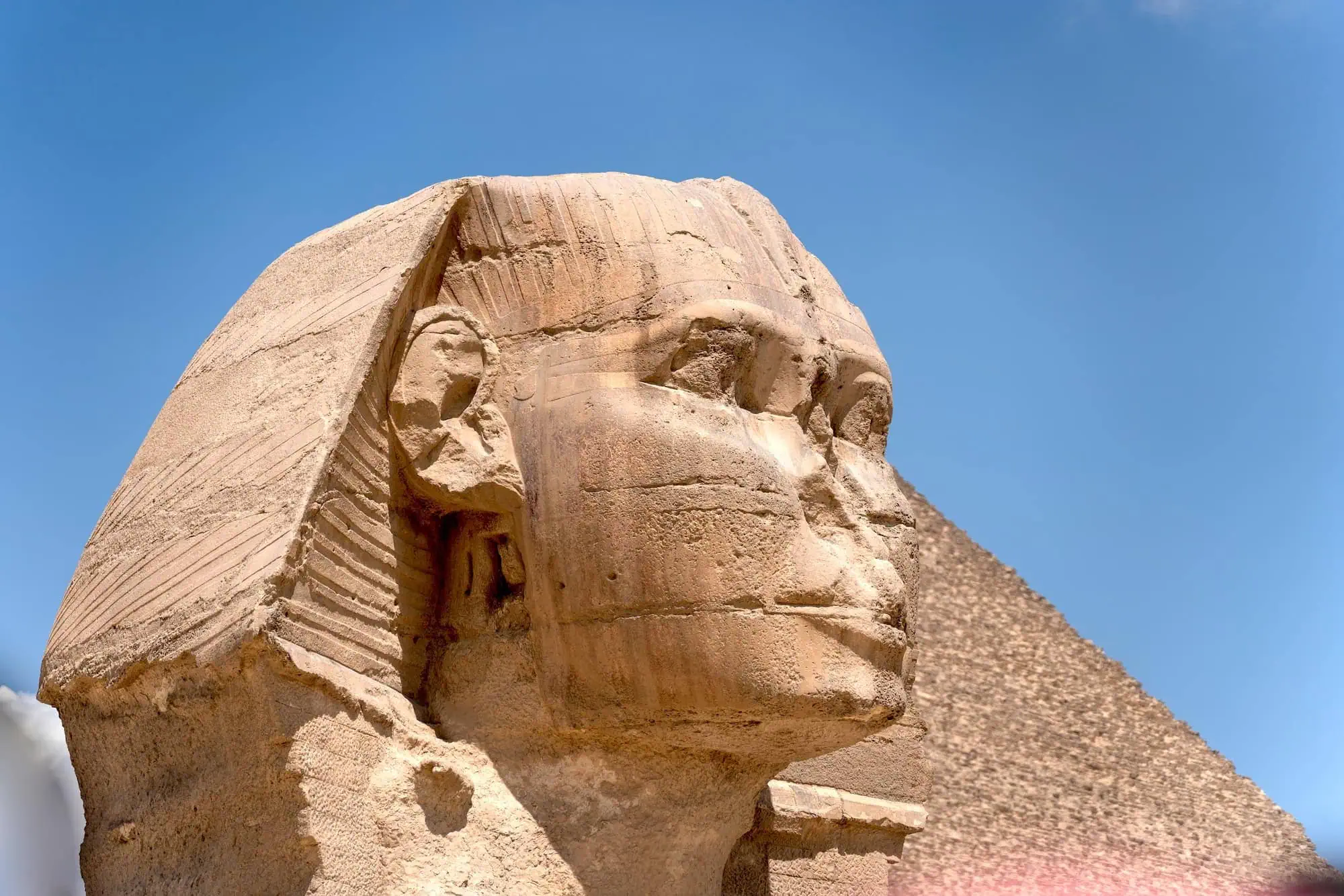 Close-up of the Great Sphinx of Giza's weathered limestone head and face against blue sky