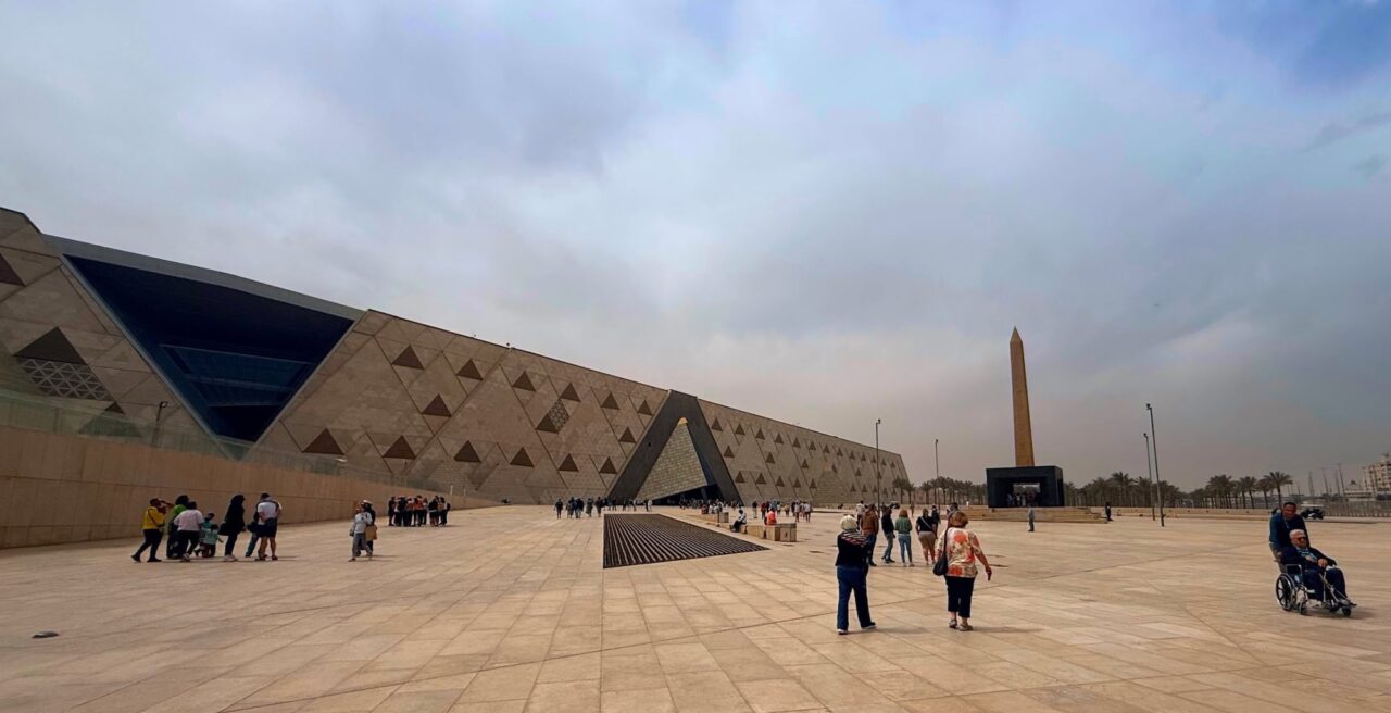 Grand Egyptian Museum entrance with a large modern facade, geometric stone walls, and a broad plaza, Giza