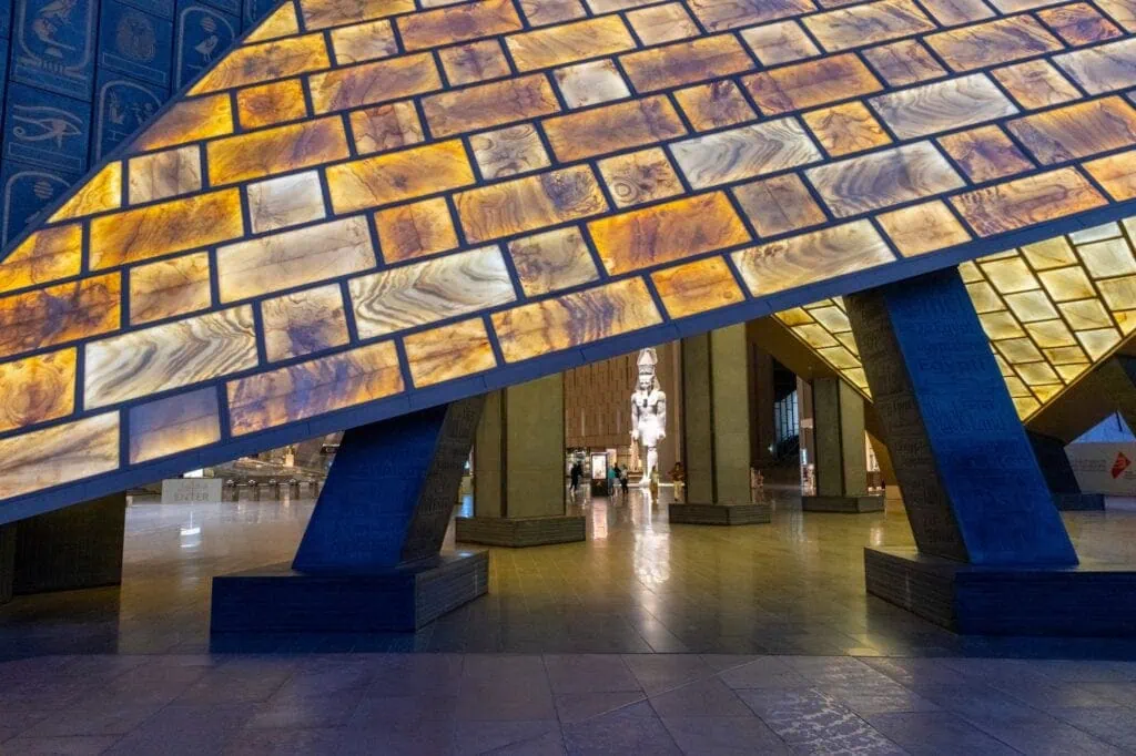 Interior hall of the Grand Egyptian Museum with pyramid-inspired architectural structure and illuminated translucent alabaster panels, Giza