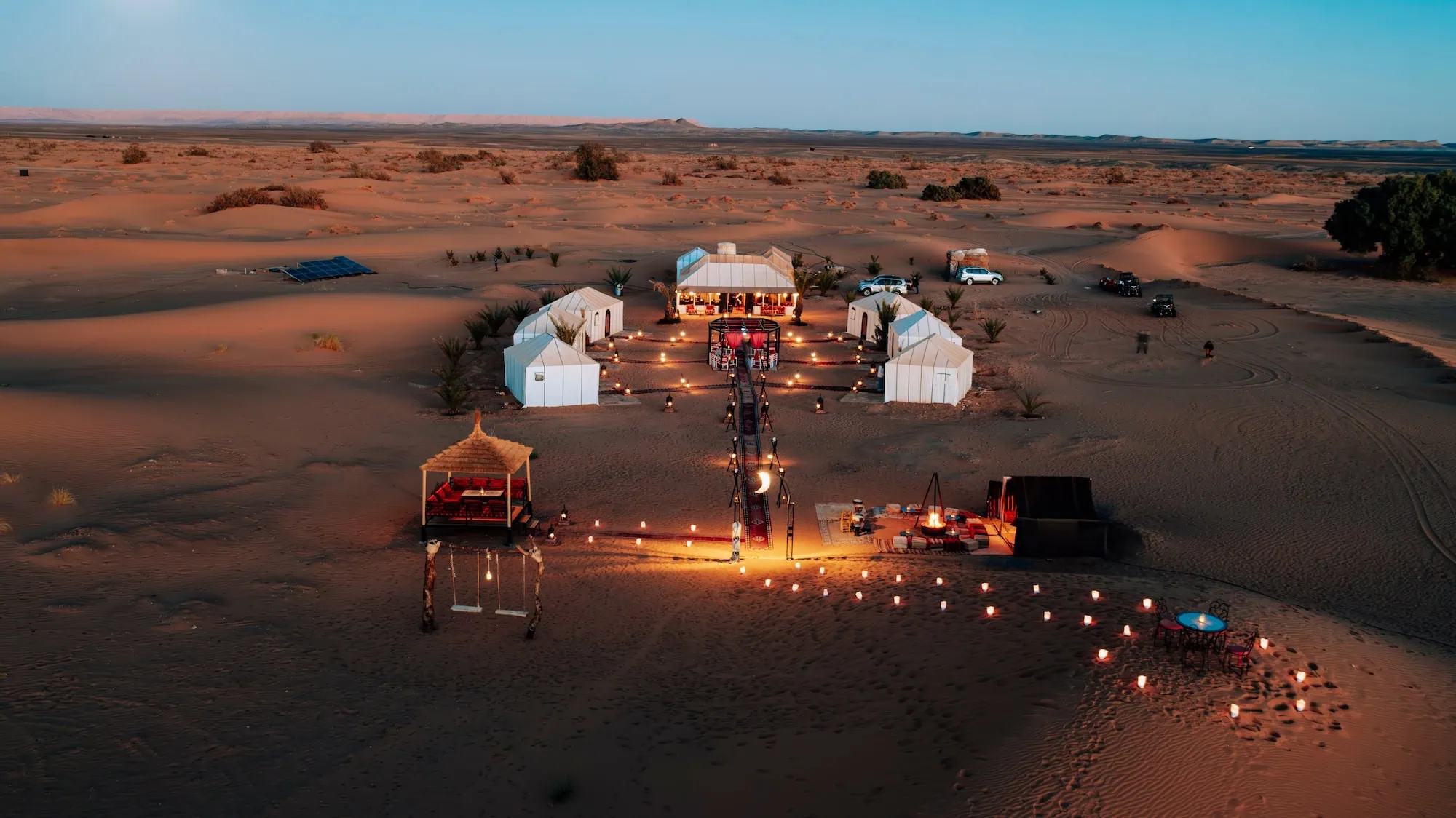 Luxury desert camp in Sahara with white tents illuminated at dusk
