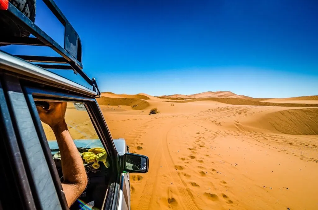 Off-road vehicle driving across sand dunes with tire tracks in Erg Chebbi desert near Merzouga