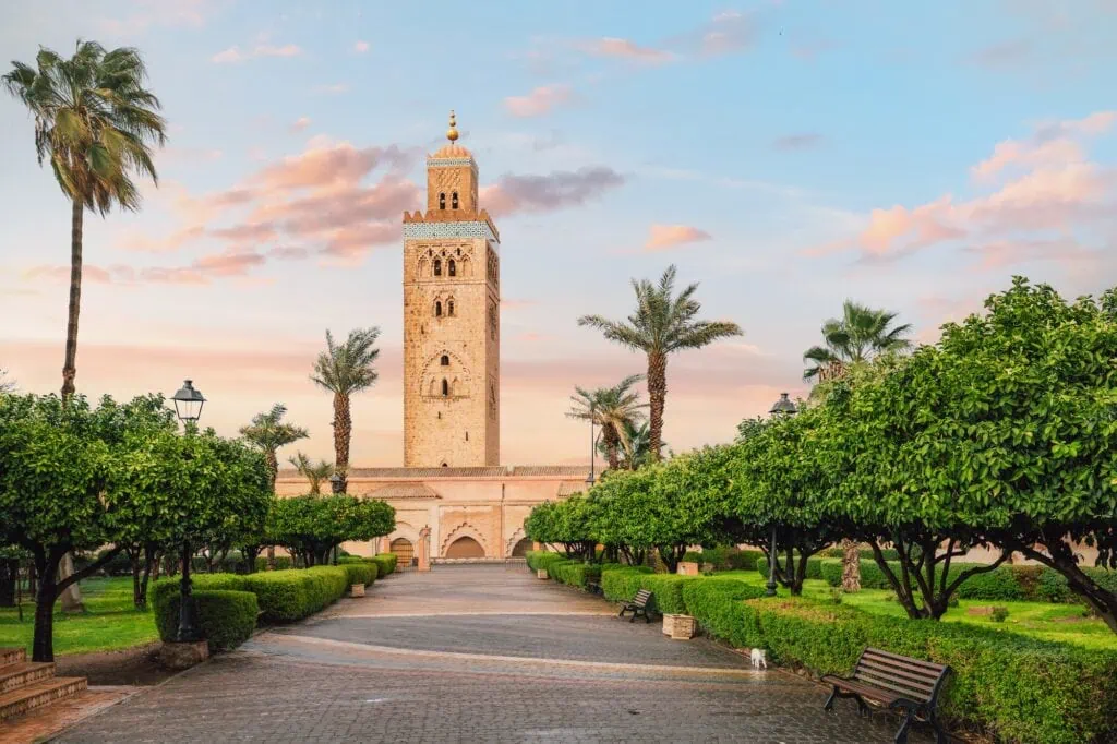 Koutoubia Mosque minaret rising above landscaped gardens with palm trees and pathways at sunset, Marrakech