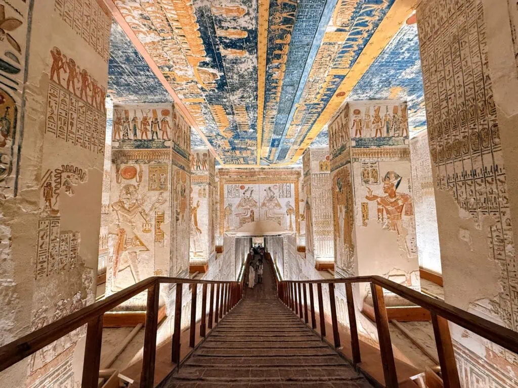 Decorated descending corridor of KV9, the Tomb of Ramesses V and Ramesses VI in the Valley of the Kings on Luxor's West Bank, with the elongated body of the sky goddess Nut painted across the vaulted ceiling depicting the Book of the Day and Book of the Night, and pillar reliefs showing Ramesses VI offering to Osiris and other deities.