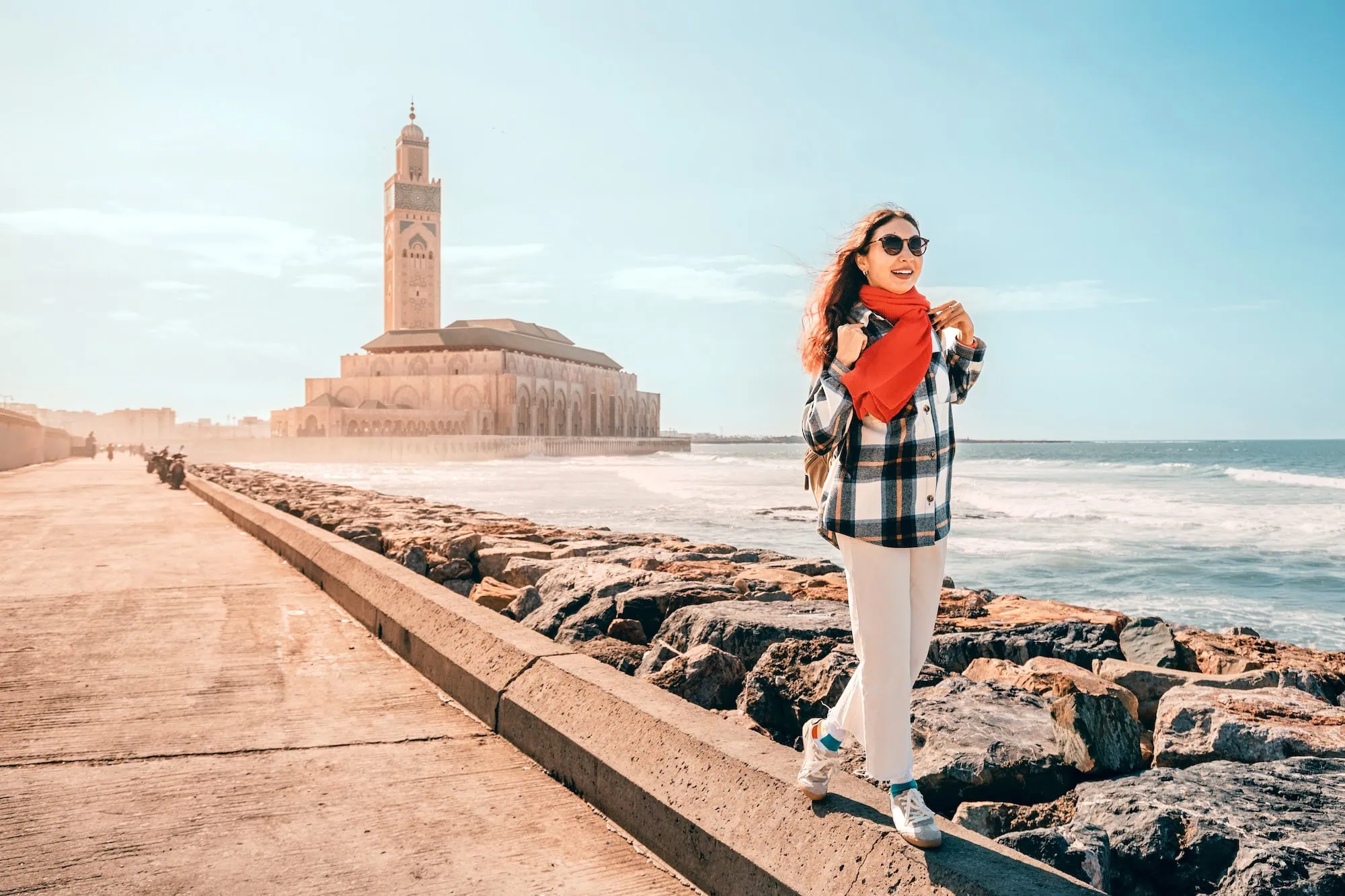 Woman walking on coastal path with Hassan II Mosque in background, Casablanca